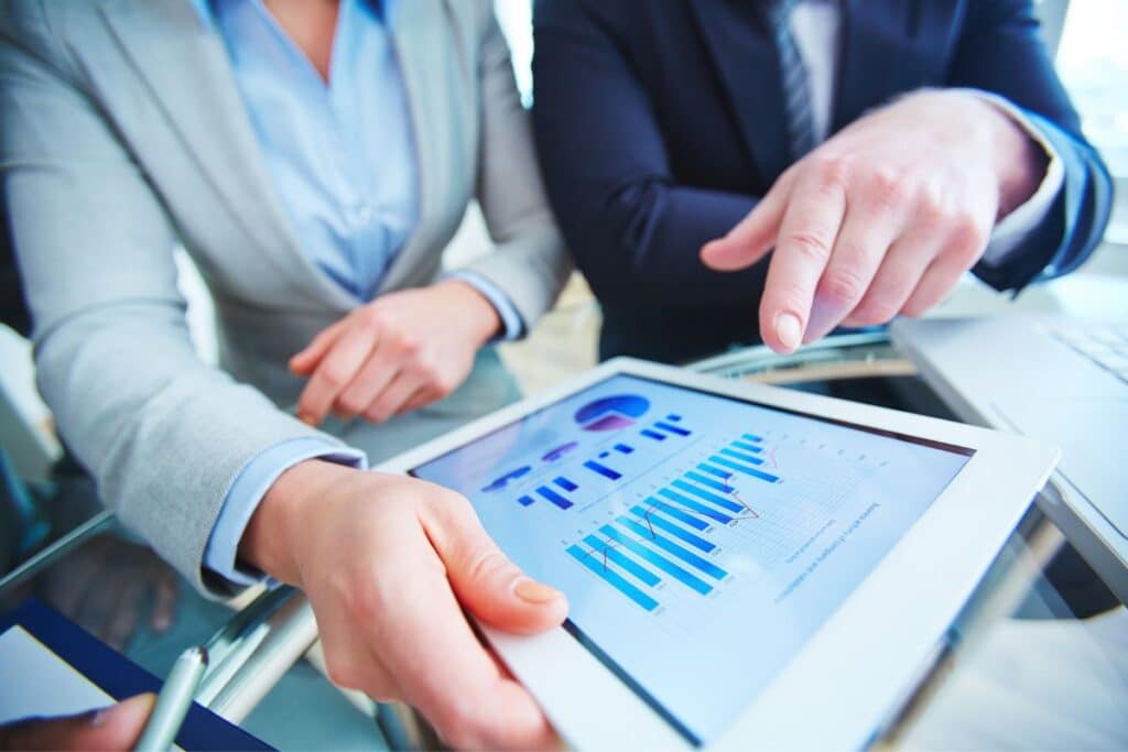 Two businesspeople review data on a tablet displaying charts, with one person pointing at the screen.