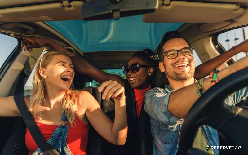 Three friends in a car, smiling and laughing together on a joyful road trip at daytime.